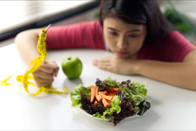 Woman looking frustrated at healthy food while holding measuring tape, representing struggles with side effects of weight loss medication